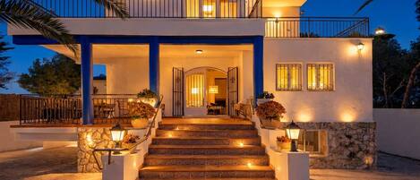 A two-story house with a stone facade, a balcony, and a staircase leading to the entrance.