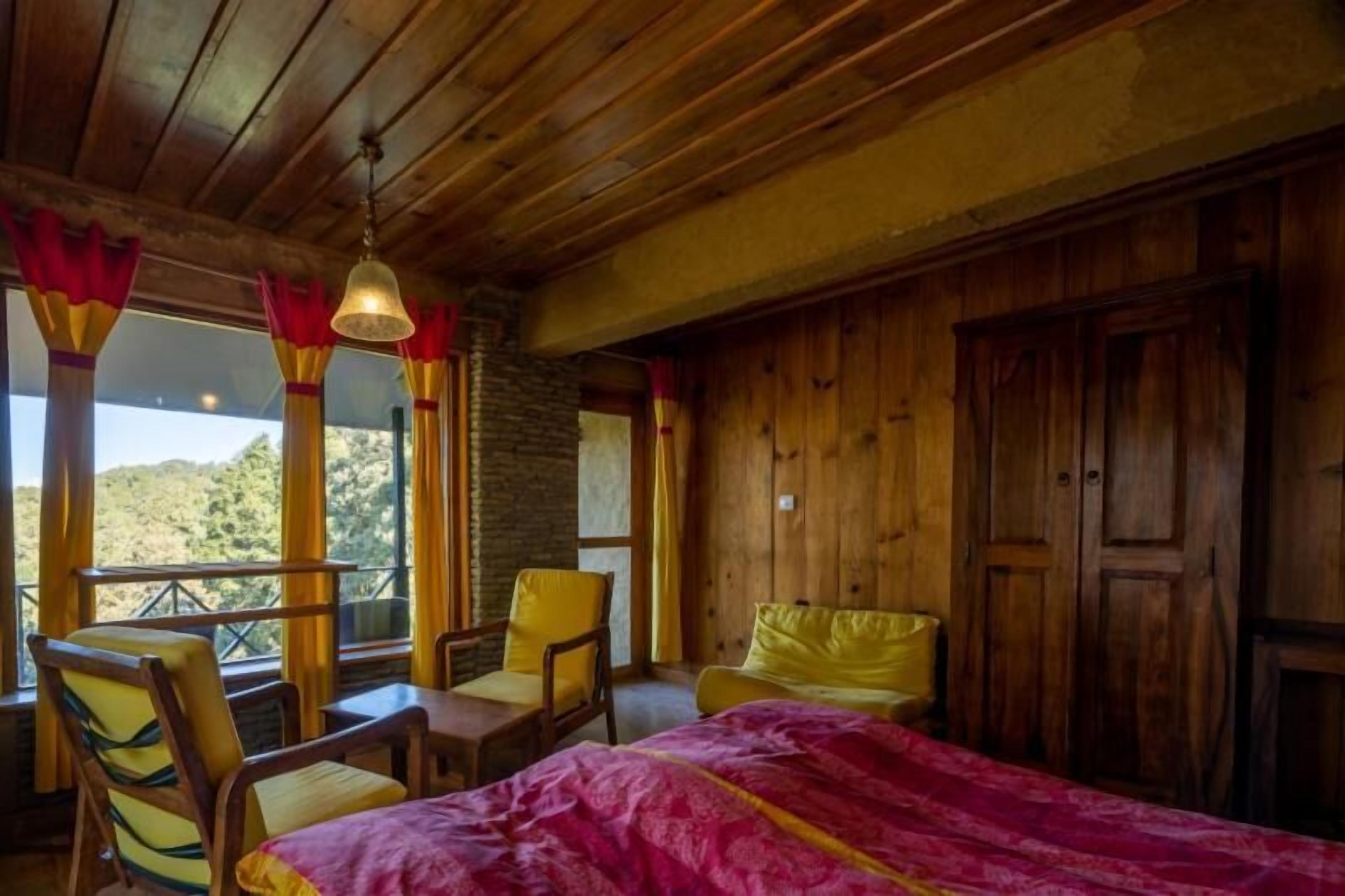 Een houten kamer met een bed, twee stoelen, een tafel en uitzicht op het omliggende landschap.