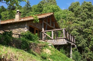 Un edificio rustico in pietra con una terrazza in legno e una scala in pietra che conduce a un ponte di legno.