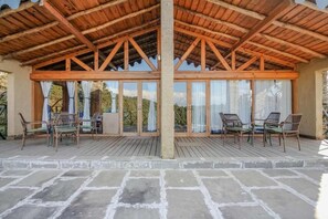 A covered outdoor seating area with chairs and a table, wooden beams, and a view of the landscape. - Binsar Forest Retreat (Binsar)