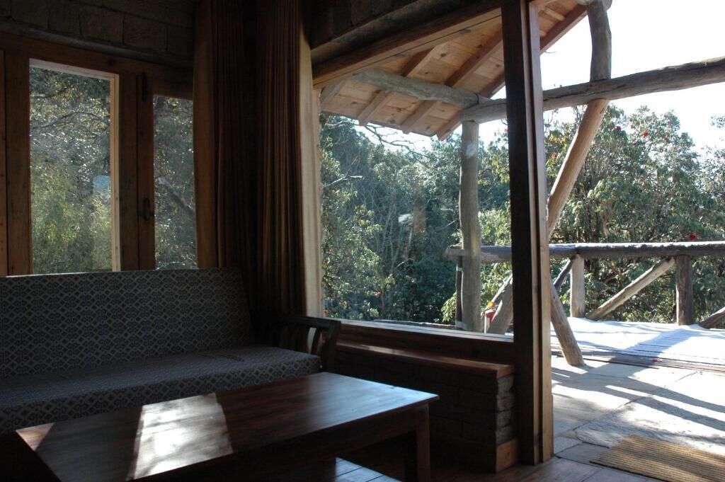 A wooden bench and table inside a room with large windows overlooking a forested area.