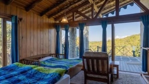 A wooden cabin with a bed, a chair, and a view of the outdoors. - Binsar Forest Retreat (Binsar)