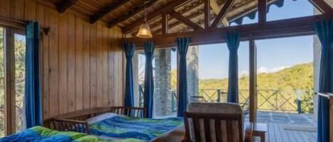 A wooden cabin with a bed, a chair, and a view of the outdoors.