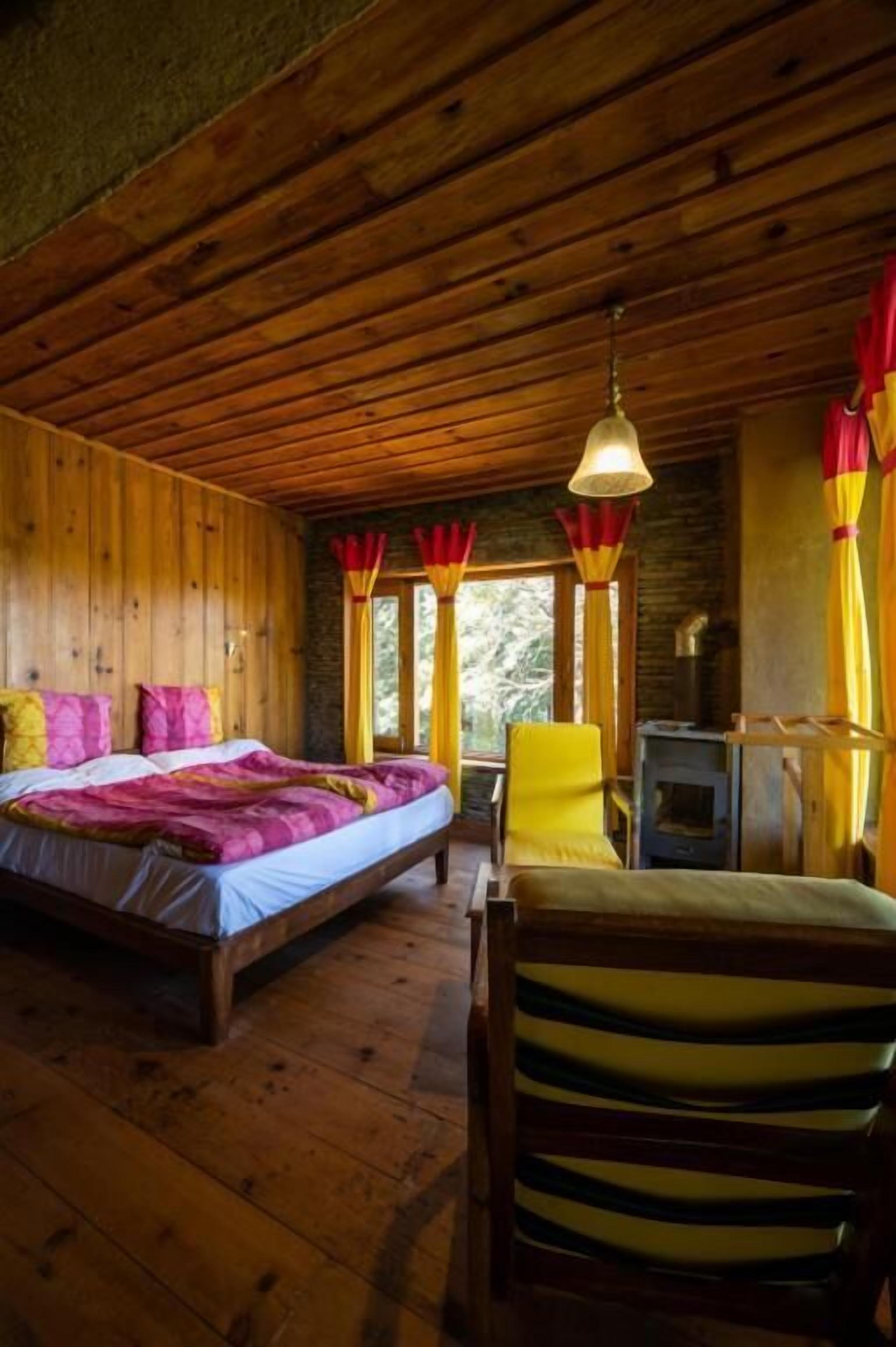A wooden cabin interior with a bed, a chair, a table, and a fireplace.