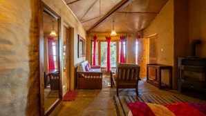 A cozy room with a wooden ceiling, a sofa, a chair, a TV, and a fireplace. - Binsar Forest Retreat (Binsar)