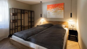 Une chambre à coucher avec un lit, deux tables de chevet, une étagère fixée au mur et un tableau.