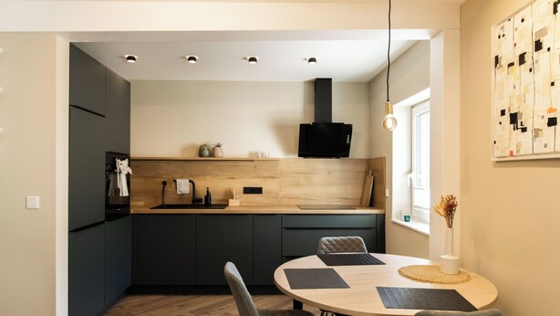 Une cuisine moderne avec des meubles de couleur sombre, un plan de travail en bois et une hotte noire.