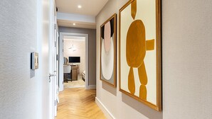 Een gang met houten vloer, een deur links en twee ingelijste abstracte schilderijen aan de rechterwand.