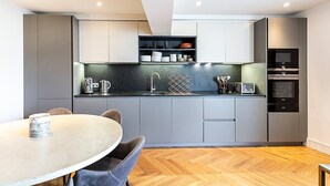 Een moderne keuken met grijze kastjes, een zwart aanrecht, een ingebouwde oven en een eethoek met een ronde tafel en stoelen.