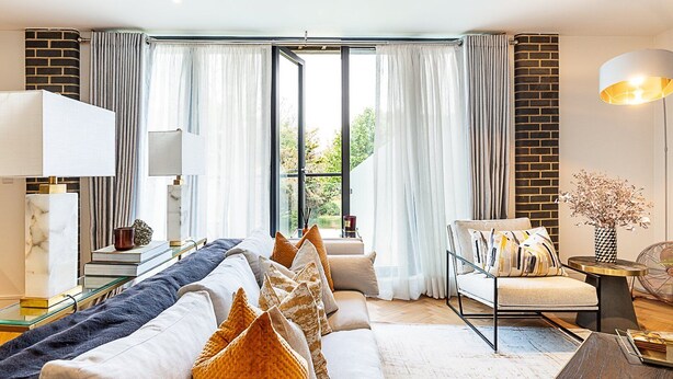 Een moderne woonkamer met een bank, een bijzettafeltje met een lamp en uitzicht door grote ramen.