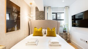 Een moderne hotelkamer met een groot bed, een flatscreen televisie, een schilderij aan de muur en een accentmuur van baksteen.