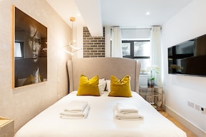 Ein modernes Hotelzimmer mit einem großen Bett, einem Flachbildfernseher, einem Gemälde an der Wand und einer Wand aus Ziegelsteinen.