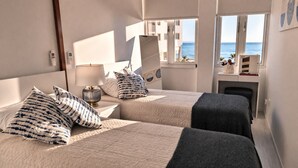Ein Hotelzimmer mit zwei Betten, einem Nachttisch, einer Lampe, einem kleinen Schreibtisch und Meerblick.