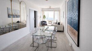 Ein stilvolles Wohnzimmer mit Esstisch aus Glas, einer Couch und einem großen abstrakten Gemälde.
