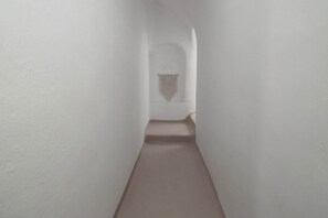 Ein schmaler, weiß getünchter Gang mit Teppichboden und einer hängenden Textilien-Dekoration am Ende.