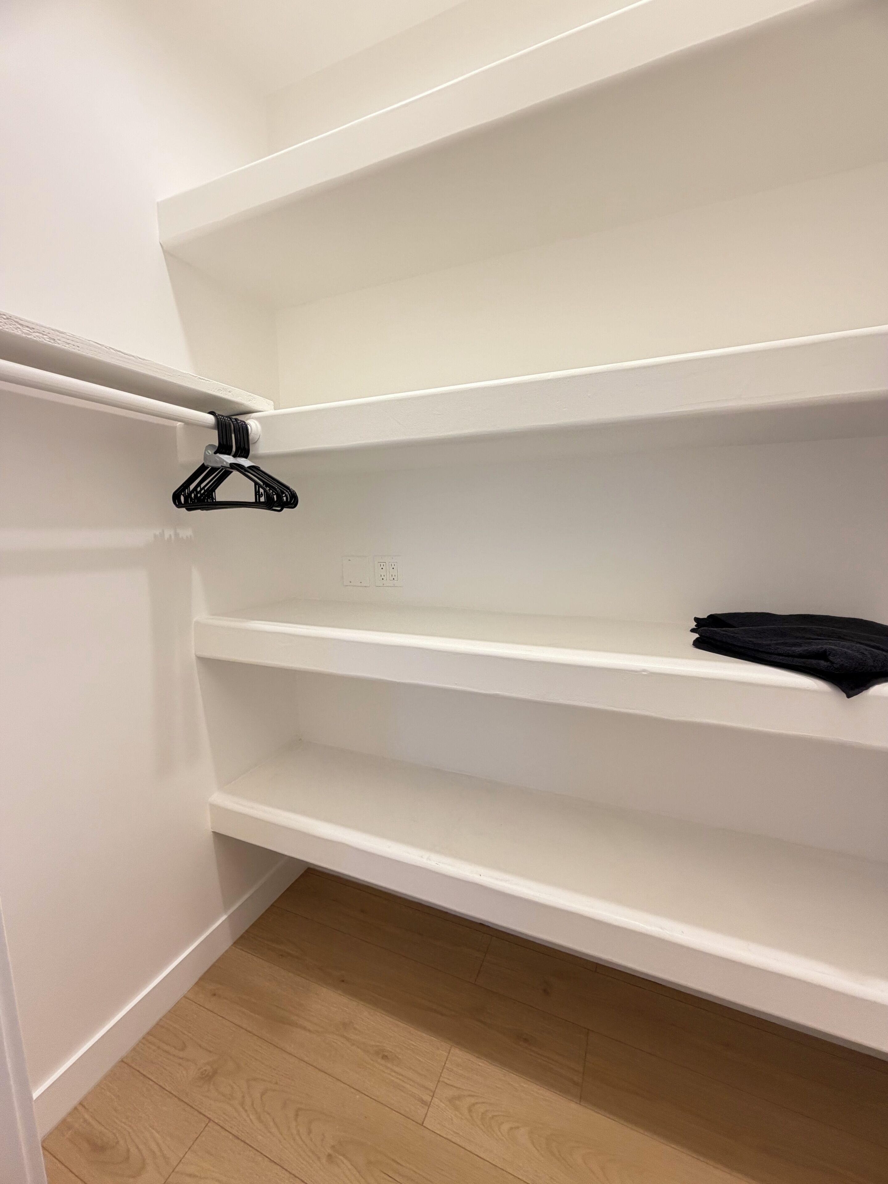 Ein weißer Kleiderschrank mit drei Einlegeböcken, einem schwarzen Kleiderbügel und einem gefalteten schwarzen Kleidungsstück auf der obersten Ablage.