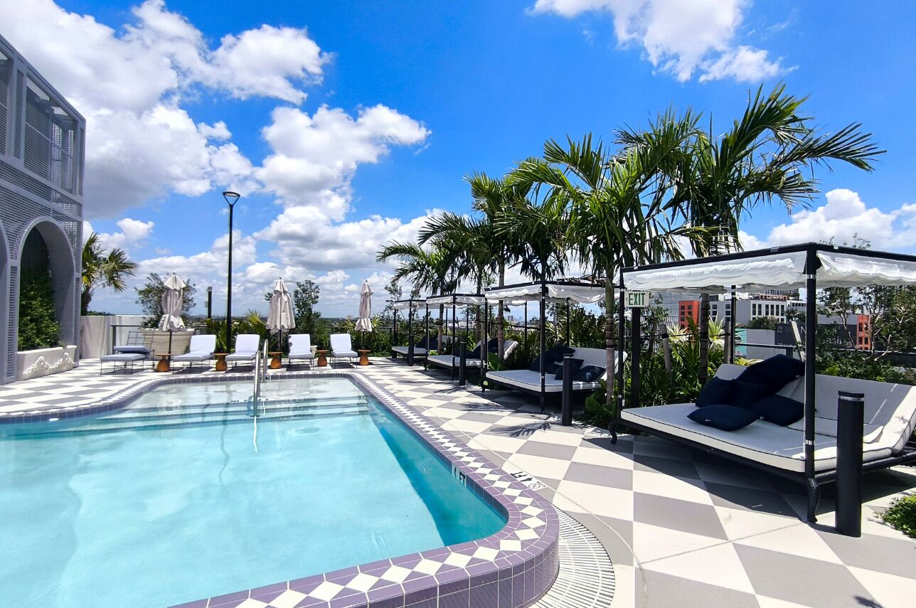 A pool area with lounge chairs, a covered seating area, and a view of the sky.