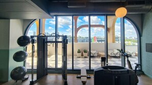 Een sportschool met trainingsapparatuur, grote ramen en uitzicht op de stad.
