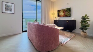 Een moderne woonkamer met een roze bank, een groot raam, een zwarte kast en een potplant.