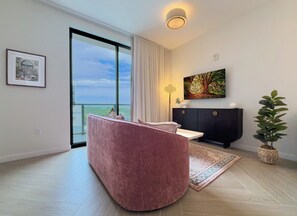 Ein modernes Wohnzimmer mit einem rosafarbenen Sofa, einem großen Fenster, einer schwarzen Kommode und einer Topfpflanze.