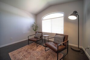 A room with a brown leather sofa, a small round table, a floor lamp, and a window with blinds.