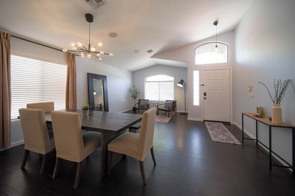 A modern living room with a dining area, dark wooden flooring, and a large window with blinds.