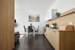 A modern kitchen with wooden cabinets, a dining area with a table and chairs, and a painting on the wall. - Air-Conditioned Apartment | Pool | Parking (Mielno)