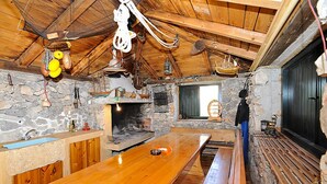 Ein rustikales Blockhaus-Interieur mit Kamin aus Stein, hölzernen Bänken und einem langen Holztisch.