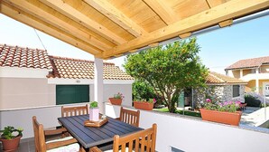 Eine Terrasse im Freien mit Holztisch und -stühlen, umgeben von Kübelpflanzen und Blick auf nahegelegene Gebäude.