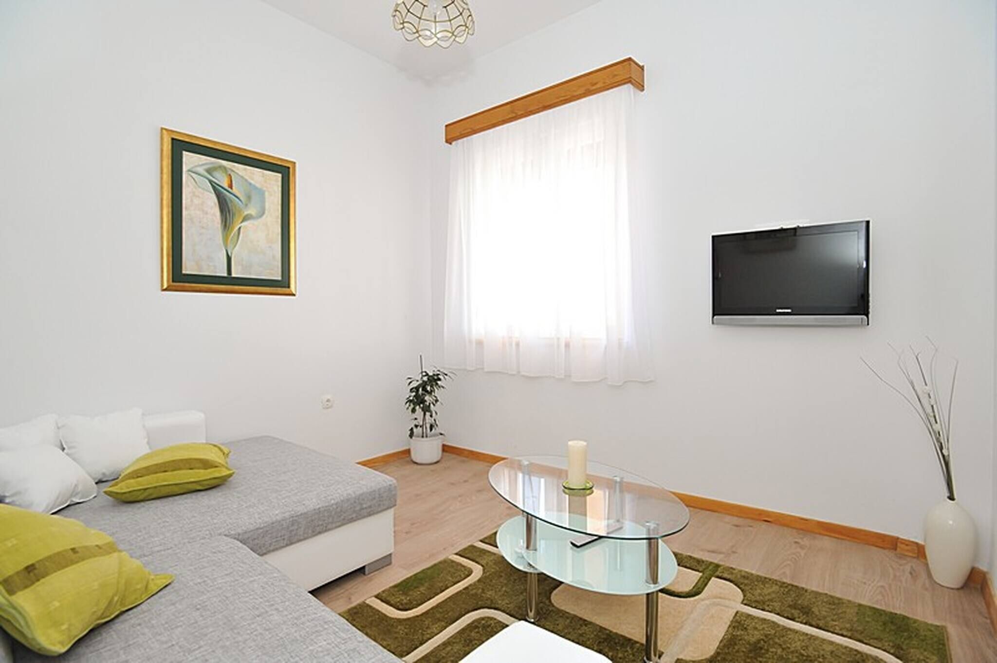 A modern living room with a sofa, a glass coffee table, a TV, and a window with curtains.