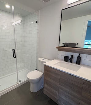 Un baño moderno con cabina de ducha de vidrio, inodoro blanco, tocador con espejo y lavabo.