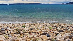 A pebble beach with clear water and a distant view of a lighthouse. - Amazing Place 4 Peaceful Holiday apartman PIA (Poljana)