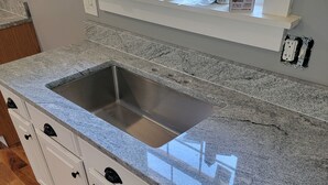 Une cuisine dotée d’un plan de travail en granit, de meubles blancs et d’une fenêtre située au-dessus de l’évier.