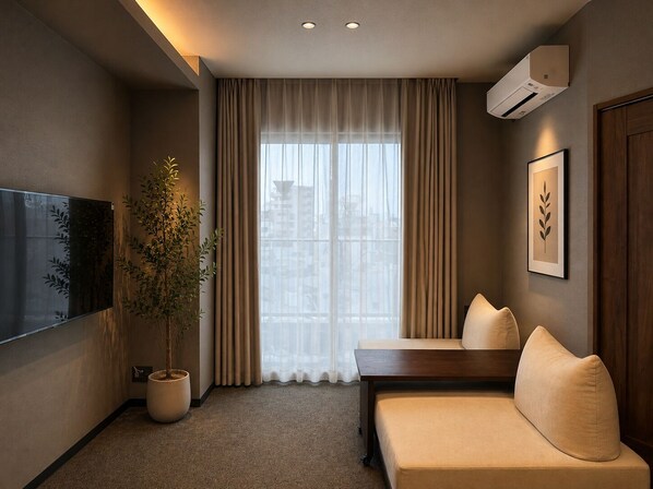 A modern hotel room with a sofa, a potted plant, a flat-screen TV, and a large window with curtains.