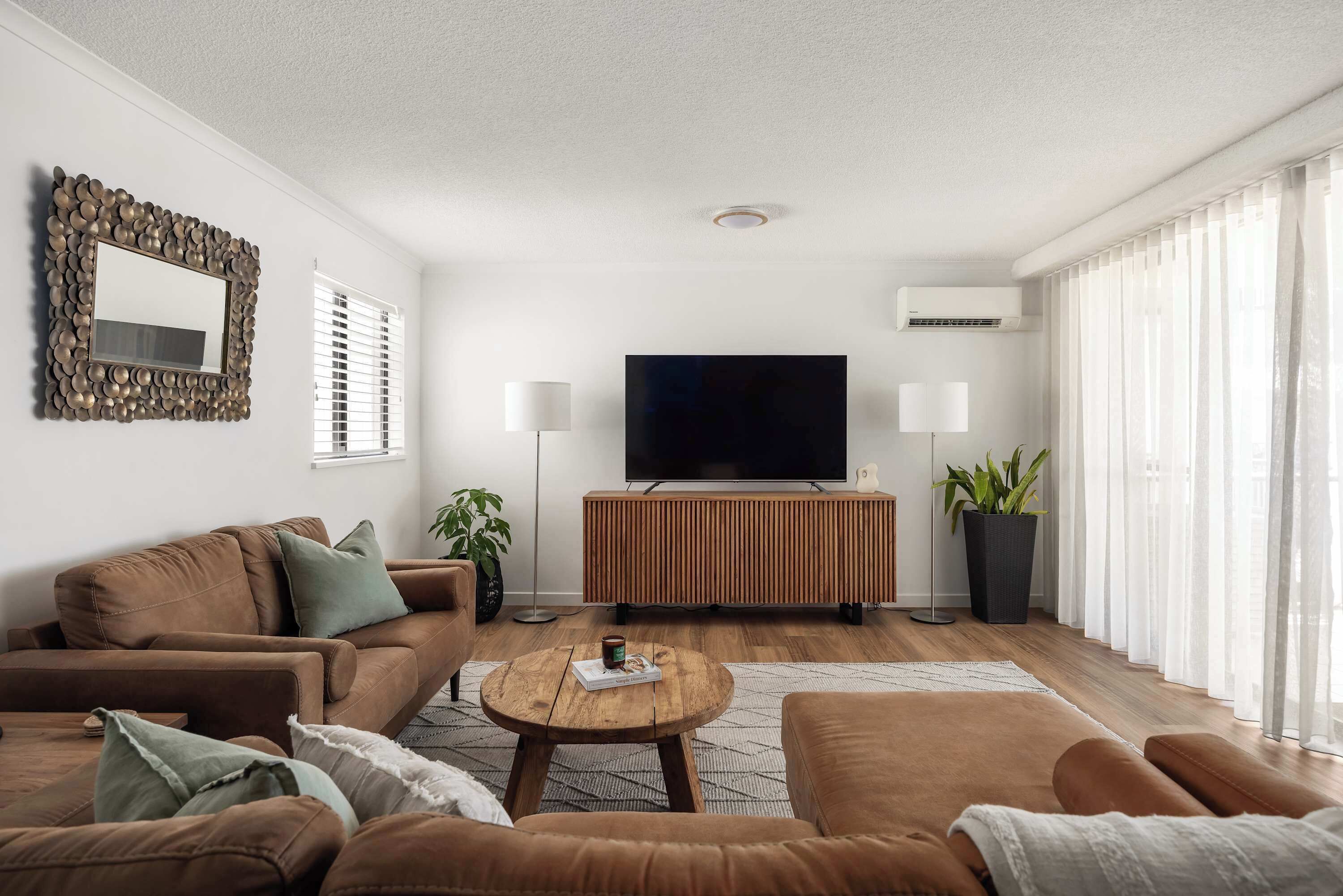 A modern living room with a sofa set, a coffee table, a flat-screen TV, and a large potted plant.
