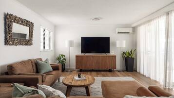 A modern living room with a sofa set, a coffee table, a flat-screen TV, and a large potted plant.