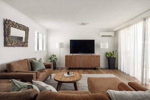 Ein modernes Wohnzimmer mit einer Sofagarnitur, einem Couchtisch, einem Flachbildfernseher und einer großen Topfpflanze.