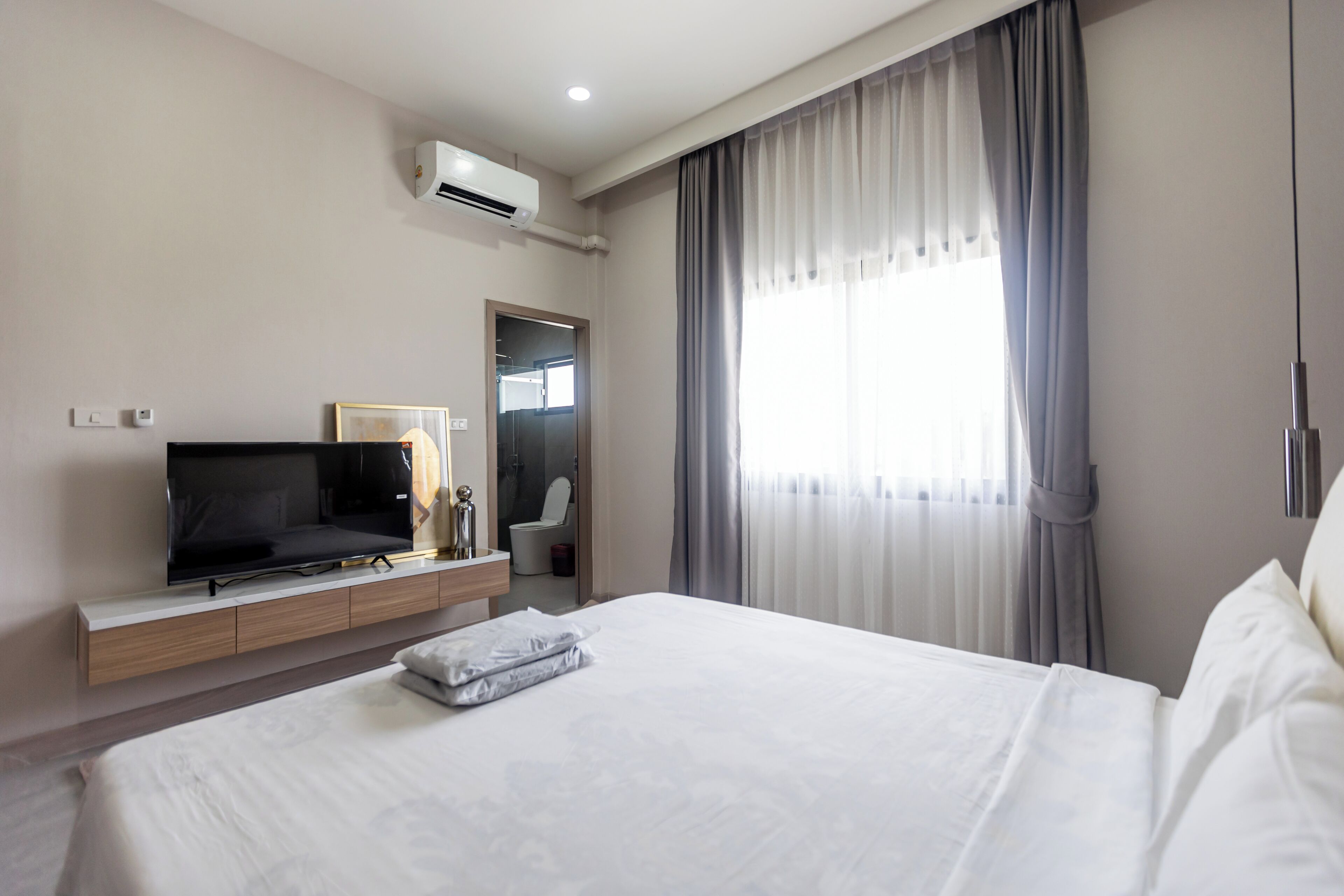 A hotel room with a bed, a TV, a bathroom, and a window with curtains.