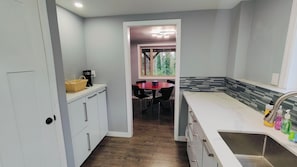 A kitchen with white cabinets, a dining table with chairs, a coffee maker, and a window with a view of trees.