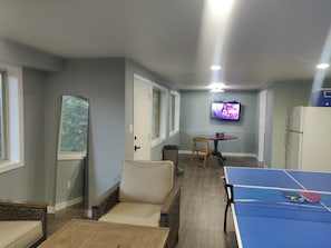 A room with a ping pong table, a television, and a dining table with chairs.