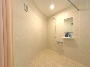 A small, tiled bathroom with a shower, a mirror, and a shelf with toiletries. - URUMA DOME Jupiter 6 (Uruma)