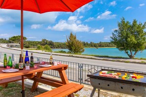 A picnic setup with a grill, table, and bottles, overlooking a body of water and a road. - URUMA DOME Jupiter 6 (Uruma)