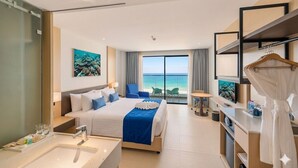 Habitación de hotel con cama, baño, escritorio, sillón, televisor y vista al océano.