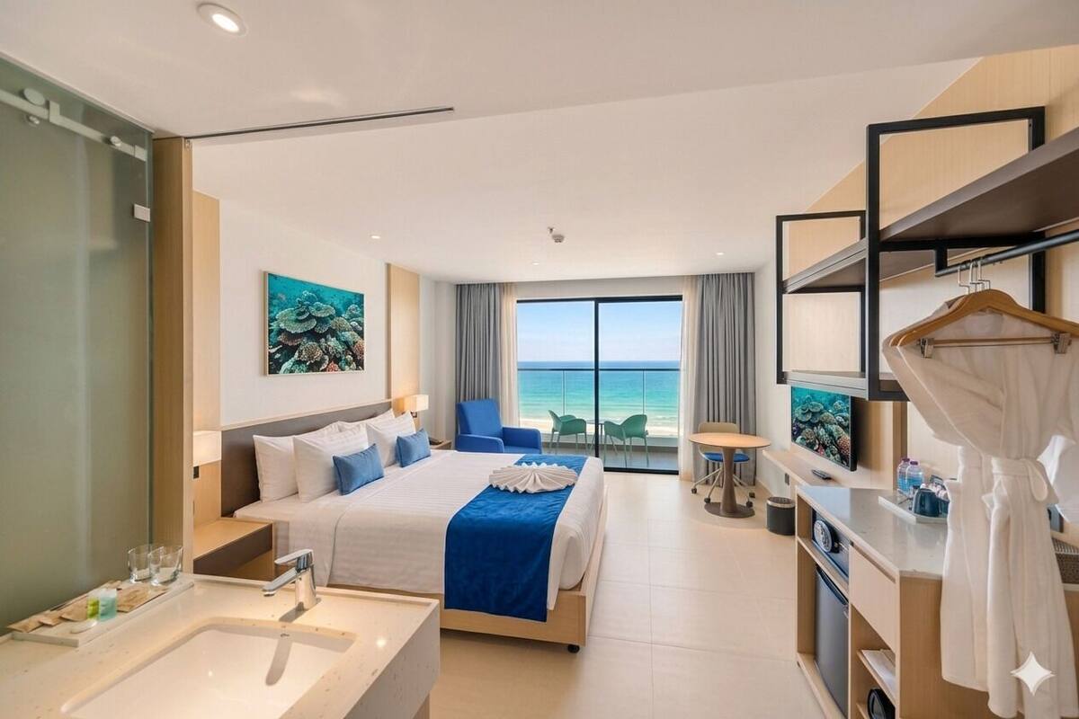Habitación de hotel con cama, baño, escritorio, sillón, televisor y vista al océano.