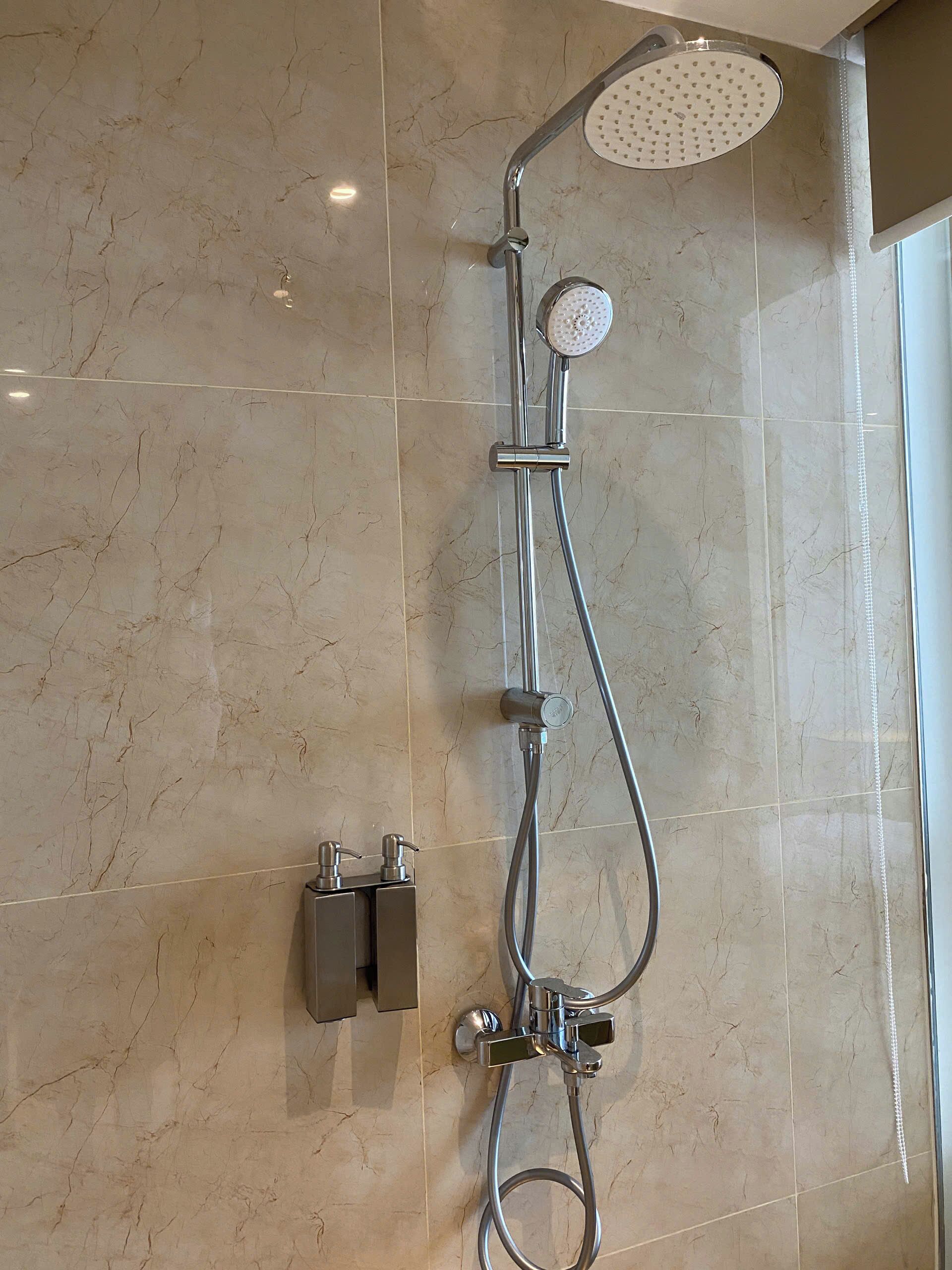 A shower with a handheld showerhead, a wall-mounted control panel, and a handheld shower attachment.