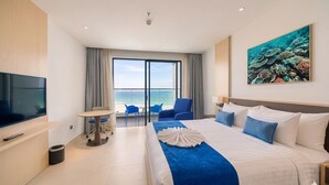 Habitación de hotel con cama, televisión, balcón con vista al océano y un cuadro de coral.