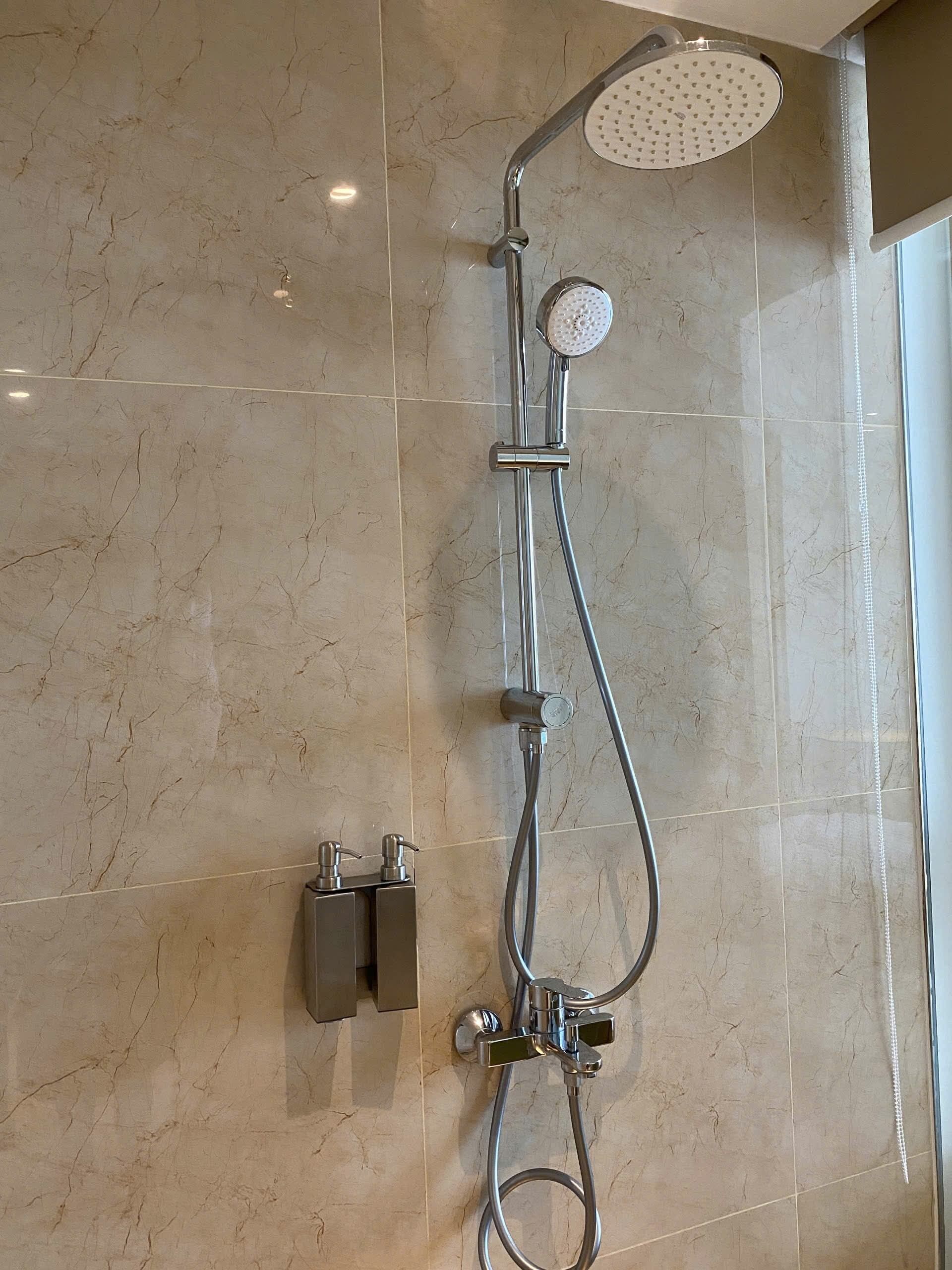 Ducha con cabezal de ducha de mano y grifo empotrado en una pared de mármol.