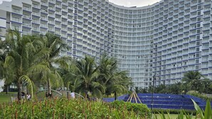 Un hotel moderno con fachada curva, exuberante vegetación y palmeras.