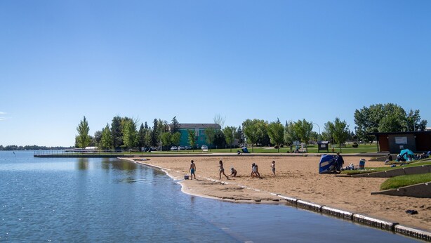 Ein See mit Strand, Personen, einem Gebäude und Bäumen.