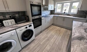 Une cuisine moderne équipée d’un lave-linge, d’un four, d’un four à micro-ondes et d’un lave-vaisselle encastré.